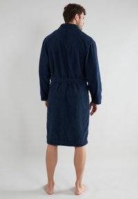 Marineblaue Frottee-Bademantel mit langen Ärmeln, einem Kragen und einem Taillengurt. Die Textur wirkt weich und saugfähig und reicht bis zur Mitte der Waden.