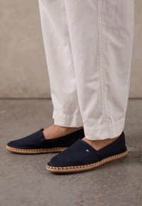 Espadrillas in tela blu navy con suola in juta intrecciata. Presentano una punta chiusa e un pannello laterale elastico. Abbinati a pantaloni bianchi leggermente affusolati.