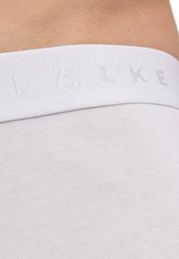 Weiße Unterwäsche aus Baumwollmischung mit einem strukturierten elastischen Bund, der den Markennamen "FALKE" in hellgrauen Buchstaben trägt. Glatte Oberfläche.