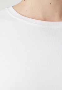Tessuto di cotone bianco a coste con scollatura a girocollo. Vista ravvicinata che evidenzia la texture e i dettagli di cucitura del colletto.