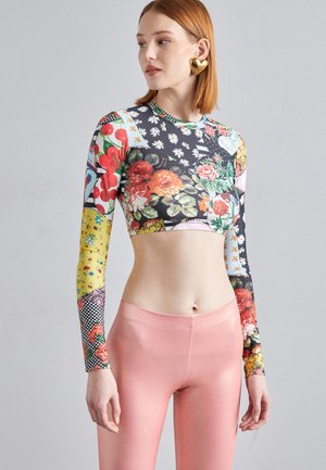 Bársonyos anyagú, élénk virágmintás crop top, hosszú ujjakkal és testhez simuló fazonnal. Magas derekú rózsaszín leggingsel párosítva.