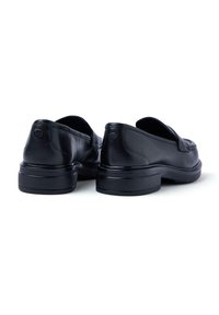Scarpe slip-on in pelle nera con punta arrotondata e suola in gomma bassa e texturizzata. La parte posteriore presenta un dettaglio del logo in rilievo. Finitura liscia in tutto.