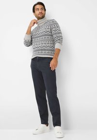 Gebreide trui met een hoge hals, gekenmerkt door een grijs en marineblauw geometrisch patroon. Gepaard met donkere broeken en witte sneakers.