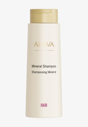 Fles AHAVA Mineral Shampoo; cilindrisch, matte crème-afwerking, gouden accenten, voorlabel toont productnaam in zwarte en roze tekst.