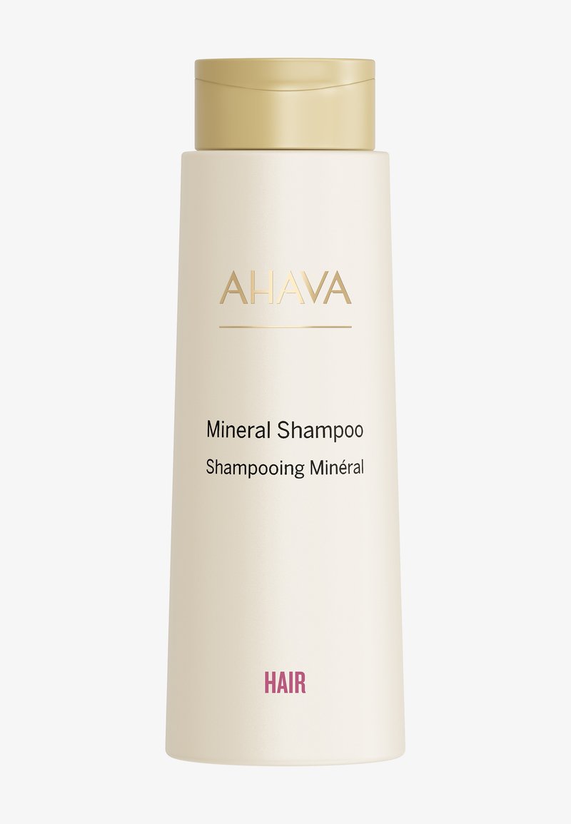Fles AHAVA Mineral Shampoo; cilindrisch, matte crème-afwerking, gouden accenten, voorlabel toont productnaam in zwarte en roze tekst.