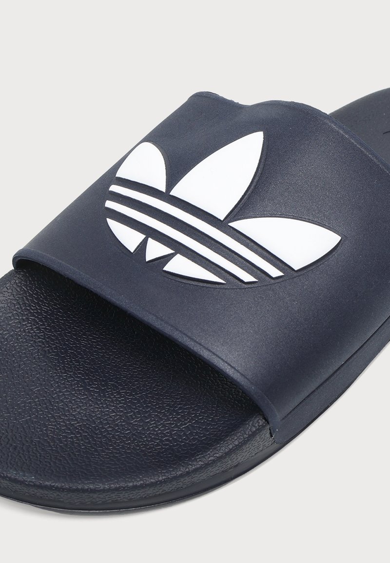 Nahaufnahme einer schwarzen Slide-Sandale mit strukturiertem Sohlenprofil und breitem Riemen mit großem weißem Adidas-Trefoil-Logo.