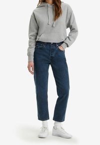 Haut en coton gris avec cordons, poche frontale ; associé à un jean en denim bleu foncé taille haute et des baskets blanches.