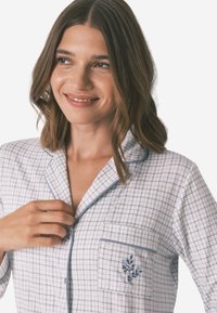 Jasnoniebieski i biały zestaw pidżamowy w kratkę z kołnierzykiem, kieszonką oraz szczegółowym haftem kwiatowym na kieszeni. Gładka tekstura materiału.