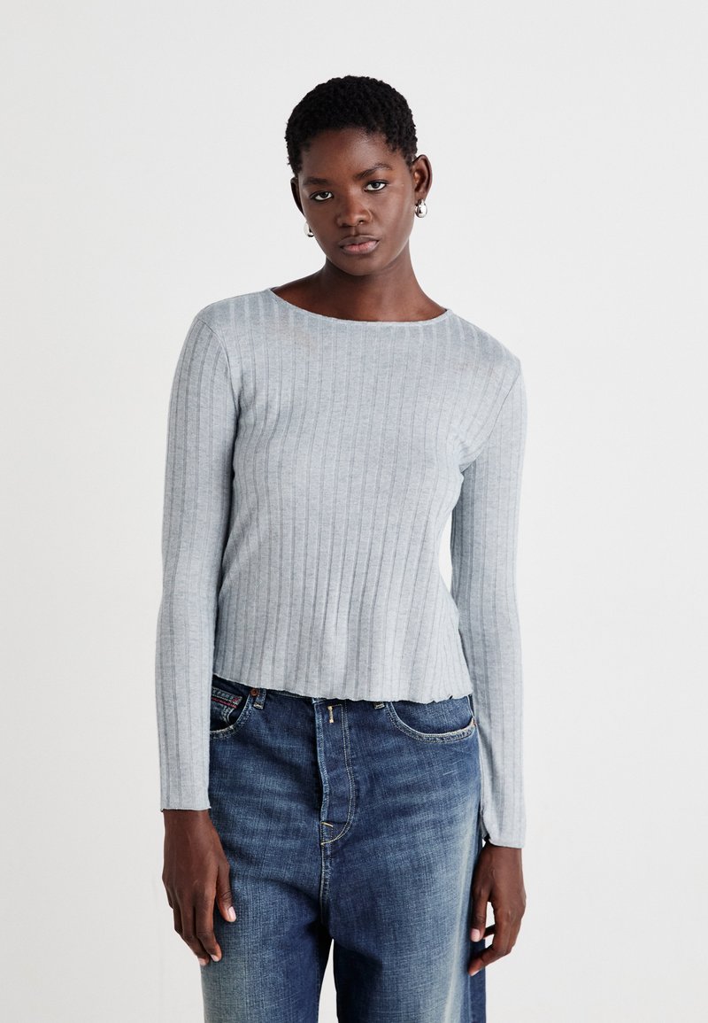 Lys grå stripete langermet topp med rund halsringning, kombinert med mørkeblå jeans. Stoffet har en myk tekstur og en tettsittende design.
