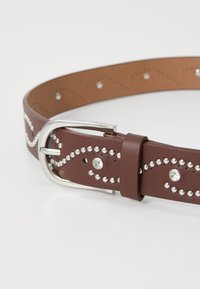 Brown leather belt with silver studs and rhinestones, featuring a silver metal buckle and a decorative wave pattern along the length.