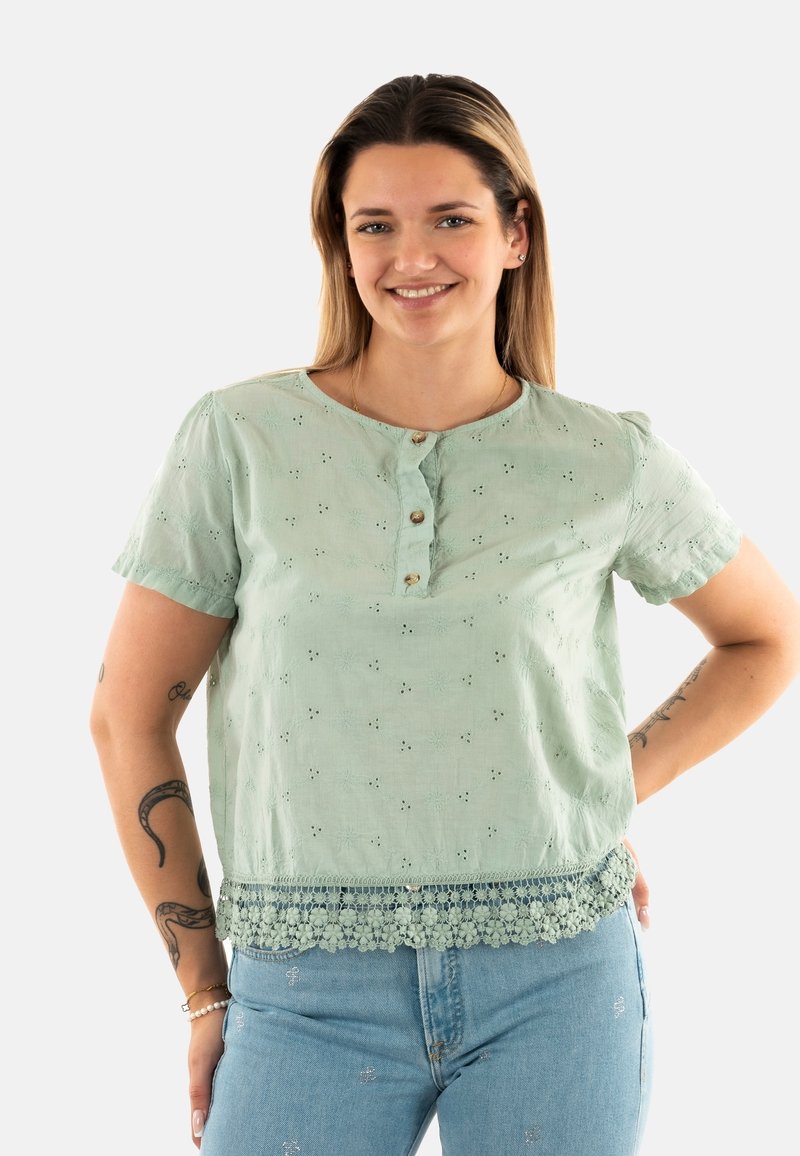 Blusa verde chiaro con maniche corte, ricamo decorativo e orlo in pizzo a forma di scallop. Presenta una patta con bottoni sul collo.