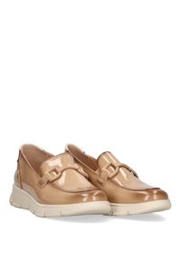 Zapatos de charol beige tipo slip-on con una correa decorativa y suela de goma blanca. Colocados uno al lado del otro sobre un fondo blanco.