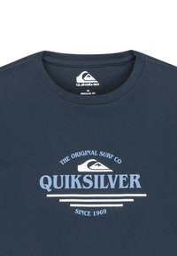T-paita tummansinistä puuvillaa, jossa Quiksilverin logo ja teksti vaaleansinisellä ja valkoisella, pyöreä pääntie ja normaalin mallin design.