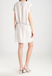 Šaty s krátkým rukávem, světlebarevné, s jemným vzorem, zúženým pasem a detaily ve tvaru klíčové dírky na zádech. V kombinaci se stříbrnými sandály na vysokém podpatku.