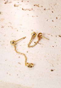 Goldene Ohrringe mit einem runden Kugeldesign, zarten Kettenverbindungen und einem einzigartigen Akzentdetail. Glatte Textur mit glänzender Oberfläche.