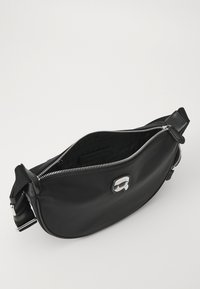 Bolso bandolera de nailon negro con cremallera y logotipo plateados. Presenta una textura suave y una forma curva, diseñado para la comodidad y el estilo.