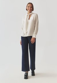 White silky blouse with a tie detail at the neckline, paired with dark blue wide-leg jeans and black loafers. Smooth texture, elegant design.