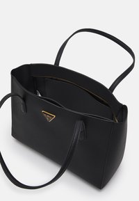 Czarna torba typu tote z teksturowanej skóry, z dwoma uchwytami, ozdobiona złotym logo z przodu oraz wewnętrzną kieszenią na zamek. Przestronna i starannie wykonana konstrukcja.