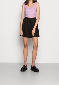 Crop top tricoté rose avec encolure carrée et ornements floraux, associé à une jupe noire fluide. Tissu transparent avec chaussures plateformes noires montant jusqu'aux chevilles.
