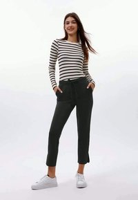 Gestreept zwart-wit langemouwshirt, gecombineerd met donkergrijze cropped broek met zijzakken en een drawstring taille, met witte schoenen.