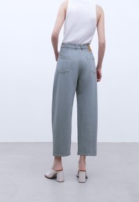 Lys grå brede bukser med høj talje, der har baglommer og et lædermærke. Bæres med beige mules med blokhæle.