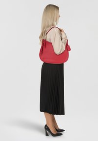 Borsa a mano in pelle rossa con finitura texturizzata e silhouette curva. Presenta una chiusura a zip e una piccola pochette abbinata attaccata.