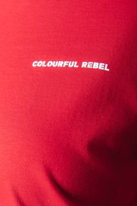 Červené bavlnené tričko s bielym textom, ktorý hovorí "KREATÍVNY REBEL." Hladká textúra s priliehavým strihom. Žiadne ďalšie vzory ani akcenty.