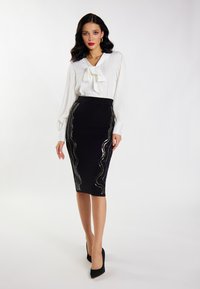Weiße Bluse mit einem Schleifenkragen, kombiniert mit einem schwarzen Bleistiftrock mit wellenförmigen silbernen Paillettenakzenten. Schwarze High Heels runden den Look ab.