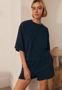 Marinblå ribbad topp med kort ärm och shorts-set. Löst snitt, mjuk textur och enkel design. I bakgrunden står en ljust färgad lampa.