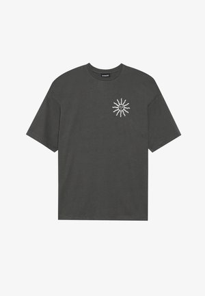 Pilkas medvilnės marškinėliai su laisvu kirpimu, turintys baltą saulės grafiką kairėje krūtinės pusėje. Trumpi rankovės ir apvalios kaklo dizainas.