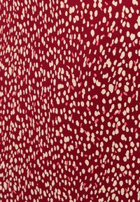 Κόκκινο ύφασμα με διάσπαρτες ακανόνιστες κρεμ και ροζ ωοειδείς κηλίδες που σχηματίζουν ένα πυκνό πουά μοτίβο.