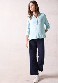 Blusa a righe blu chiaro con maniche lunghe e scollatura con bottoni abbinata a jeans svasati blu scuro e sneakers bianche.