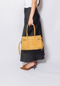 Borsa a tracolla gialla in suede con manici in pelle, caratterizzata da una forma strutturata, cuciture a contrasto e un piccolo tassello attaccato.