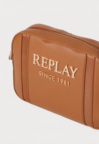 Brun syntetisk lærveske med rektangulær form, med preget tekst "REPLAY SINCE 1981" og gullfarget glidelås.