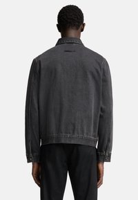 Svart denimjacka, avslappnad passform, med kontrasterande sömmar, klassisk krage och knappmanchetter. Har en ok och en enfärgad baksida.