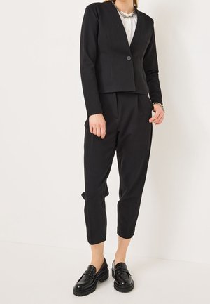 Sort skræddersyet blazer med V-hals, enkelt knaplukning, kombineret med matchende cropped bukser og polerede sorte loafers.