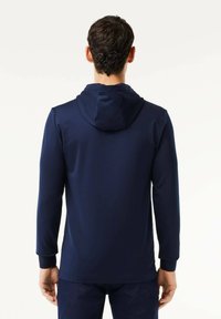 Marinblå huoodie i slät väv, med långa ärmar, dragsko i huoodien och en figurnära design. Inga synliga mönster.