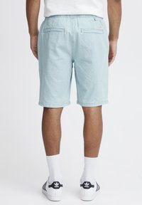 Lyseblå shorts med elastisk midje, to baklommer og rullet kant. Brukt med hvite sokker og svarte stribede sneakers.