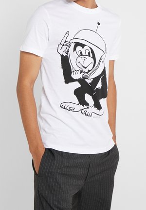 Mann trägt weißes T-Shirt mit schwarzem Cartoon-Affen im Astronautenhelm, der vorne eine Friedensgeste macht.