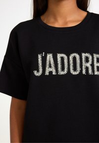 Sort kortærmet t-shirt med "J'ADORE" tekst prydet med rhinsten, med rund halsudskæring og en afslappet pasform.