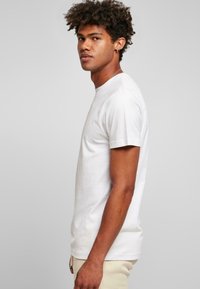 Tricou alb din bumbac, cu guler rotund și mâneci scurte, prezentat pe un model în profil lateral, pe un fundal neutru.