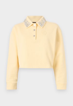 Skraťená žltá mikina s dlhými rukávmi, ozdobený golier s gombíkmi so striebornými korálkami, tri gombíky na prednej strane a vyšívané logo.