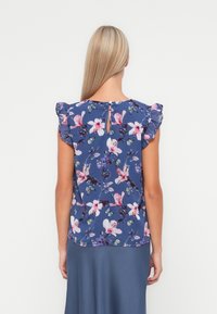 Marinblå kortärmad topp med blommönster, volangaxlar och nyckelhålöppning bak, med rosa och gröna accentfärger.