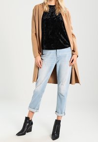 Beige lang frakke, sort fløjlstop, lyseblå slidte jeans og sorte ankelstøvler. Bløde teksturer og kontrasterende farver.