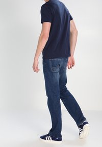 Navyblå bomullströja, blå denimjeans med rak benstil, och blå sneakers med vita ränder. Avslappnad outfit sedd bakifrån.