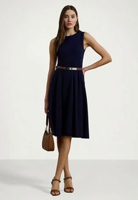 Ναυτικό αμάνικο φόρεμα με εφαρμοστό μπούστο και φουσκωτό παντελόνι, σφιγμένο στη μέση με ζώνη. Συνδυάζεται με καφέ σανδάλια και τσάντα.