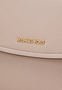 Gros plan sur du cuir texturé beige avec le logo doré "Michael Kors" et une couture visible sur l'accessoire.