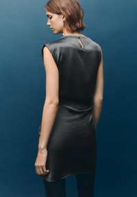 Vestido de satén negro con un detalle de ojal en la espalda, diseño sin mangas y un ajuste suavemente drapeado, todo ello sobre un fondo azul.