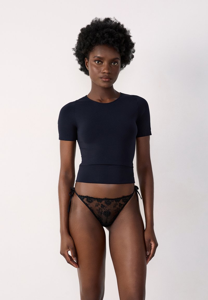 Haut ajusté à manches courtes bleu marine associé à un string en dentelle noire avec des motifs floraux et des liens sur les côtés. Texture lisse sur l'ensemble.