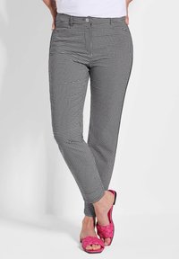 Pantalons à carreaux noir et blanc avec une coupe slim, dotés de poches avant et d'une texture lisse, associés à des sandales à glissière en rose tressé.